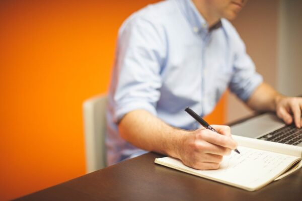 Man writing in a notebook and typing on a laptop