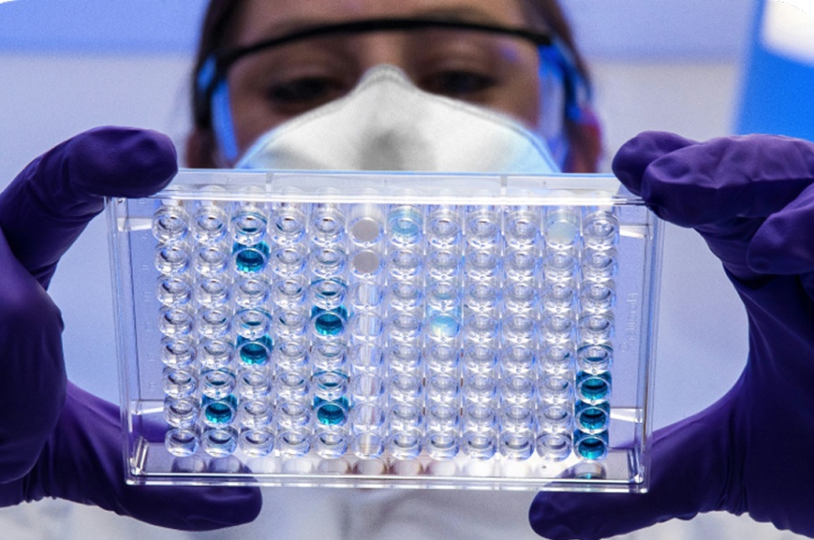 A researcher with goggles and a facemask looking at substances in a tray
