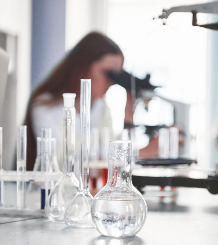clear beakers with clear fluid in them and a girl in the background looking through a microscope
